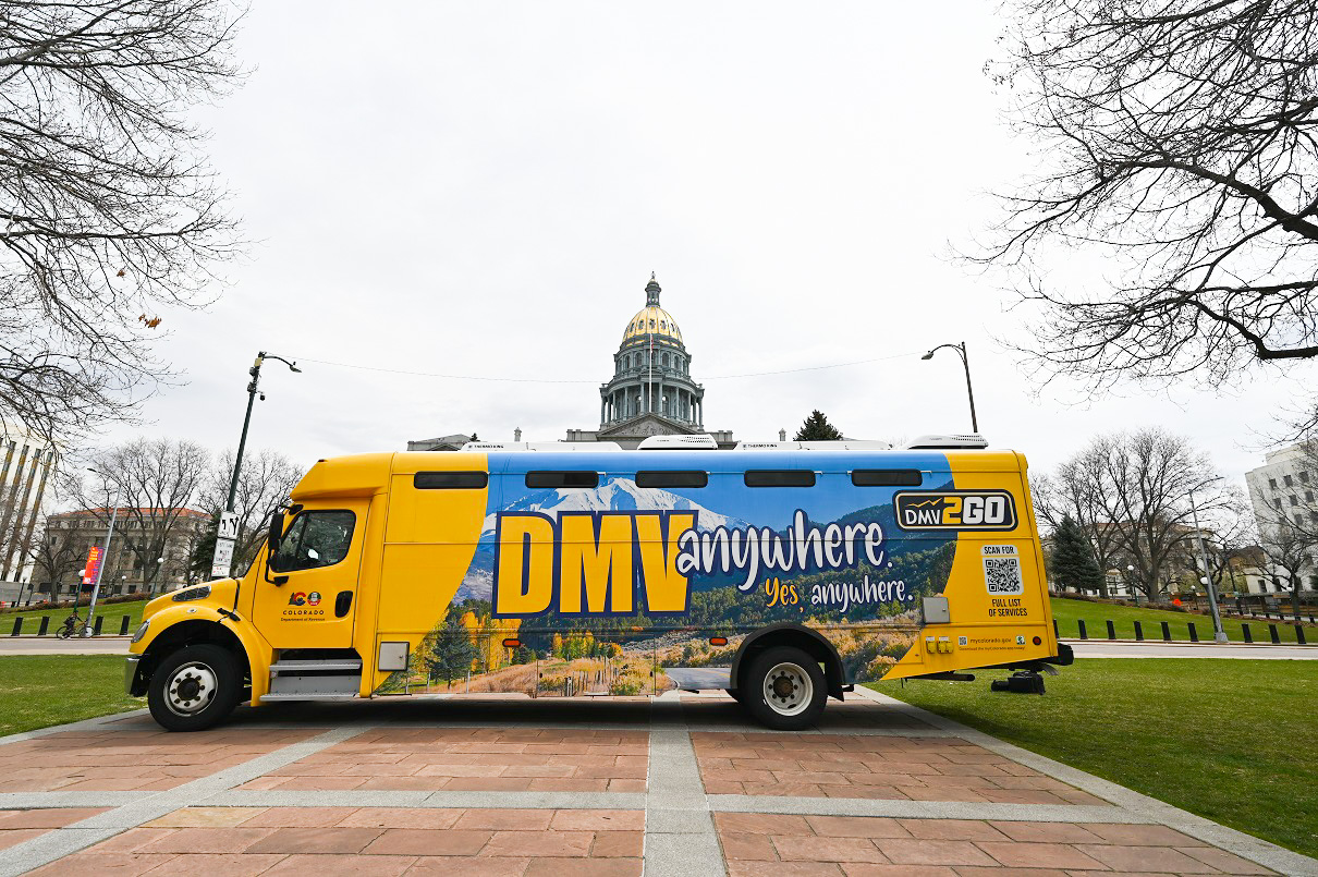 yellow bus with DMV branding is parked in front of Colorado State Capitol
