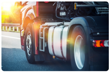 Semi truck driving down road with sunburst coming through trees